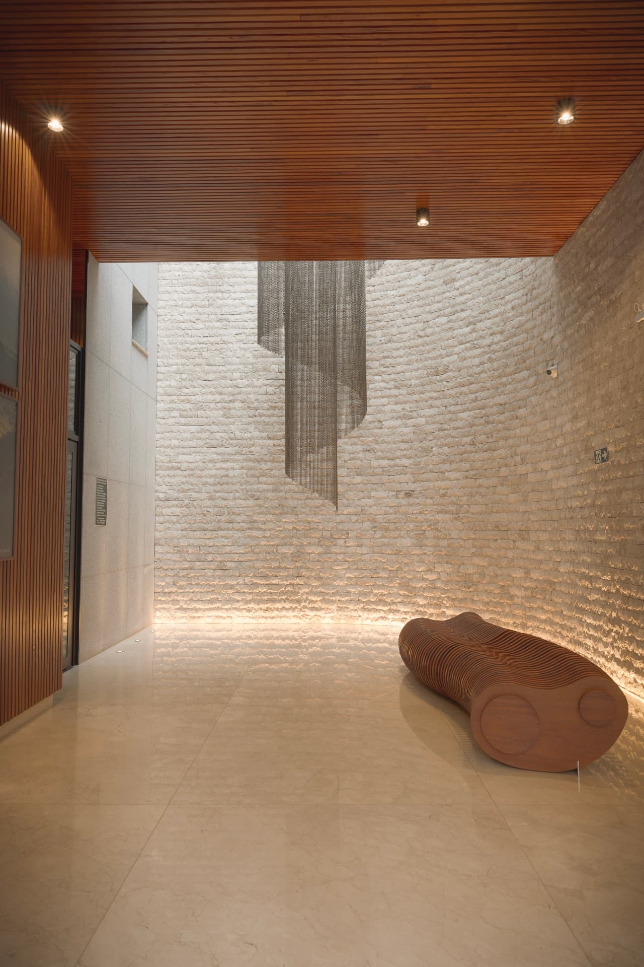 Hall de entrada com pé-direito alto, revestimento em pedra, luminária pendente e forro de madeira